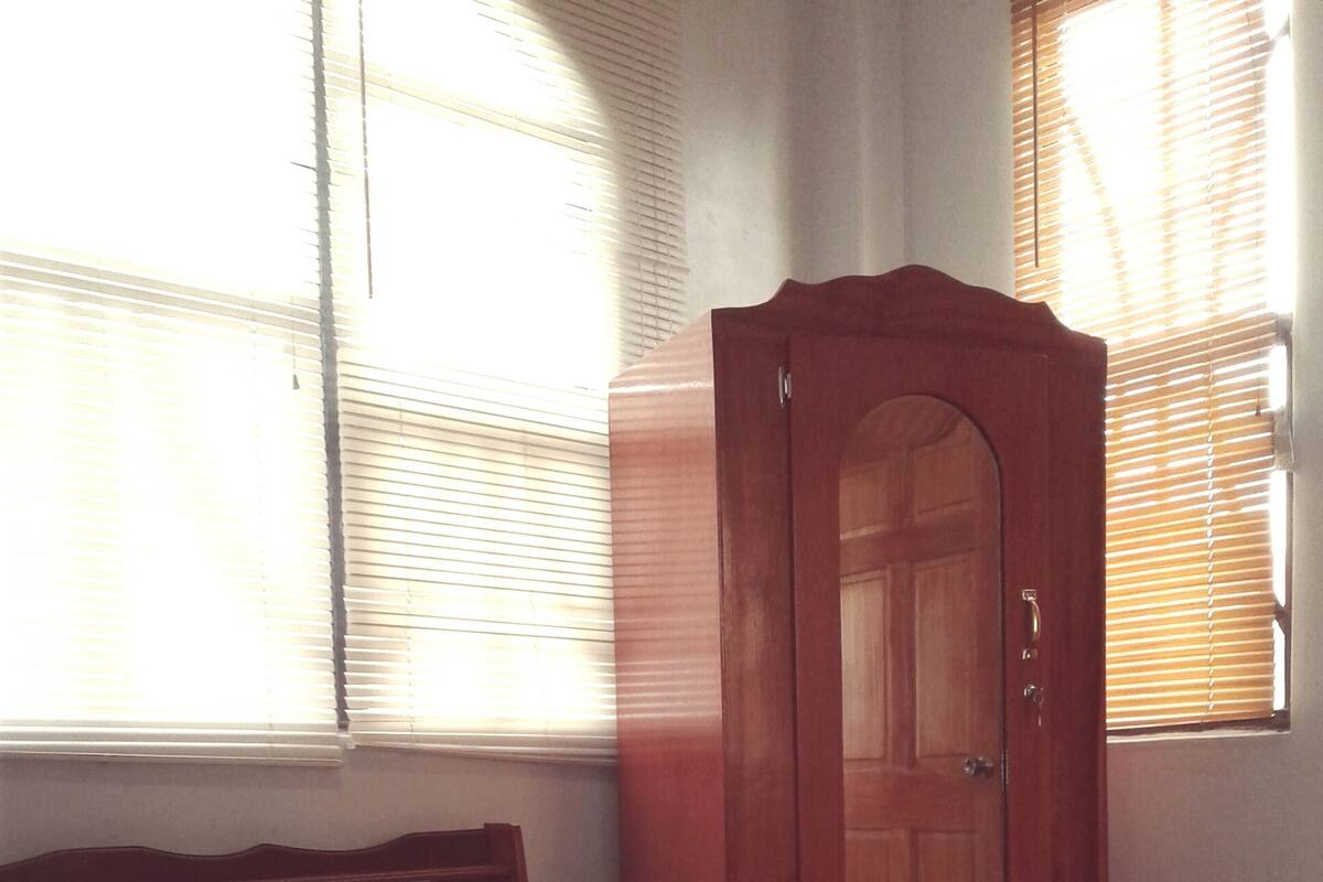 A bedroom with a bed, a wooden wardrobe, and a window with blinds.