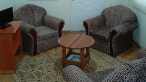 Un salón con sillones estampados, una mesa de centro de madera y una puerta con diseño decorativo.