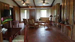 Een ruime woonkamer met houten wanden en plafond, een eethoek met tafel en stoelen, en een bank.