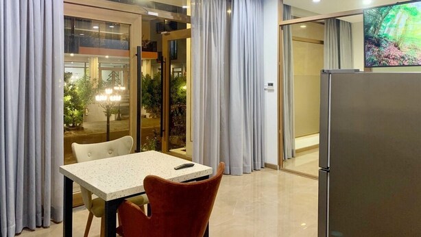 Une chambre d’hôtel moderne dotée d’un coin repas, d’une grande fenêtre avec des rideaux, d’un réfrigérateur et d’un écran de télévision diffusant des images de la nature.