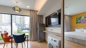 Une chambre d’hôtel moderne dotée d’une grande fenêtre, d’un téléviseur à écran plat, d’un lave-linge, d’un lit et d’un coin repas avec des chaises.