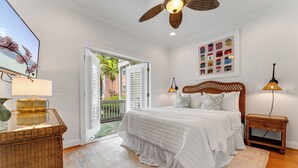 Une chambre à coucher comprenant un lit, une table de chevet, une lampe, un ventilateur de plafond et une vue sur l’extérieur.