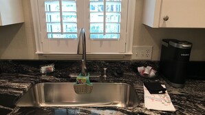 A kitchen with a stainless steel sink, a Keurig coffee maker, and a window with a view of greenery.