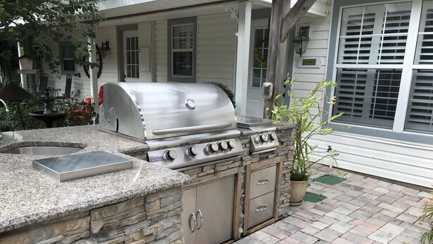 An outdoor kitchen with a built-in grill, stone counter, and a potted plant.