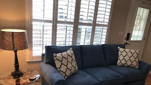 A living room with a blue sofa, patterned cushions, a glass coffee table, and a lamp.