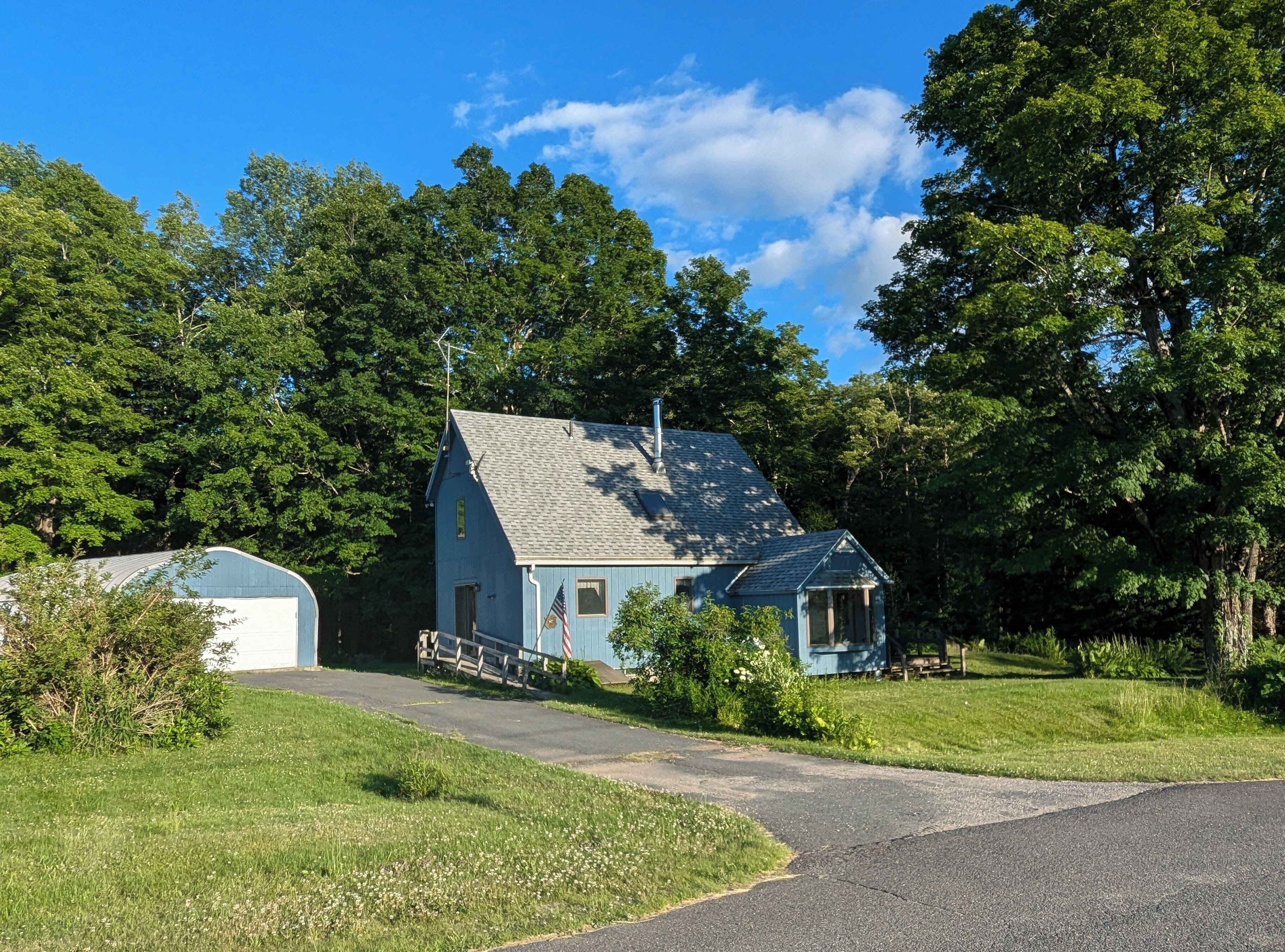 A small, single-story building with a sloped roof, surrounded by lush greenery and trees.