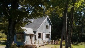 A two-story wooden house with a porch and a large window on the ground floor.