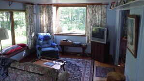 A living room with a blue armchair, a sofa, a television, and a window with curtains.