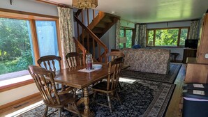A spacious living room with a wooden dining table, chairs, a large rug, and a staircase leading to an upper level.
