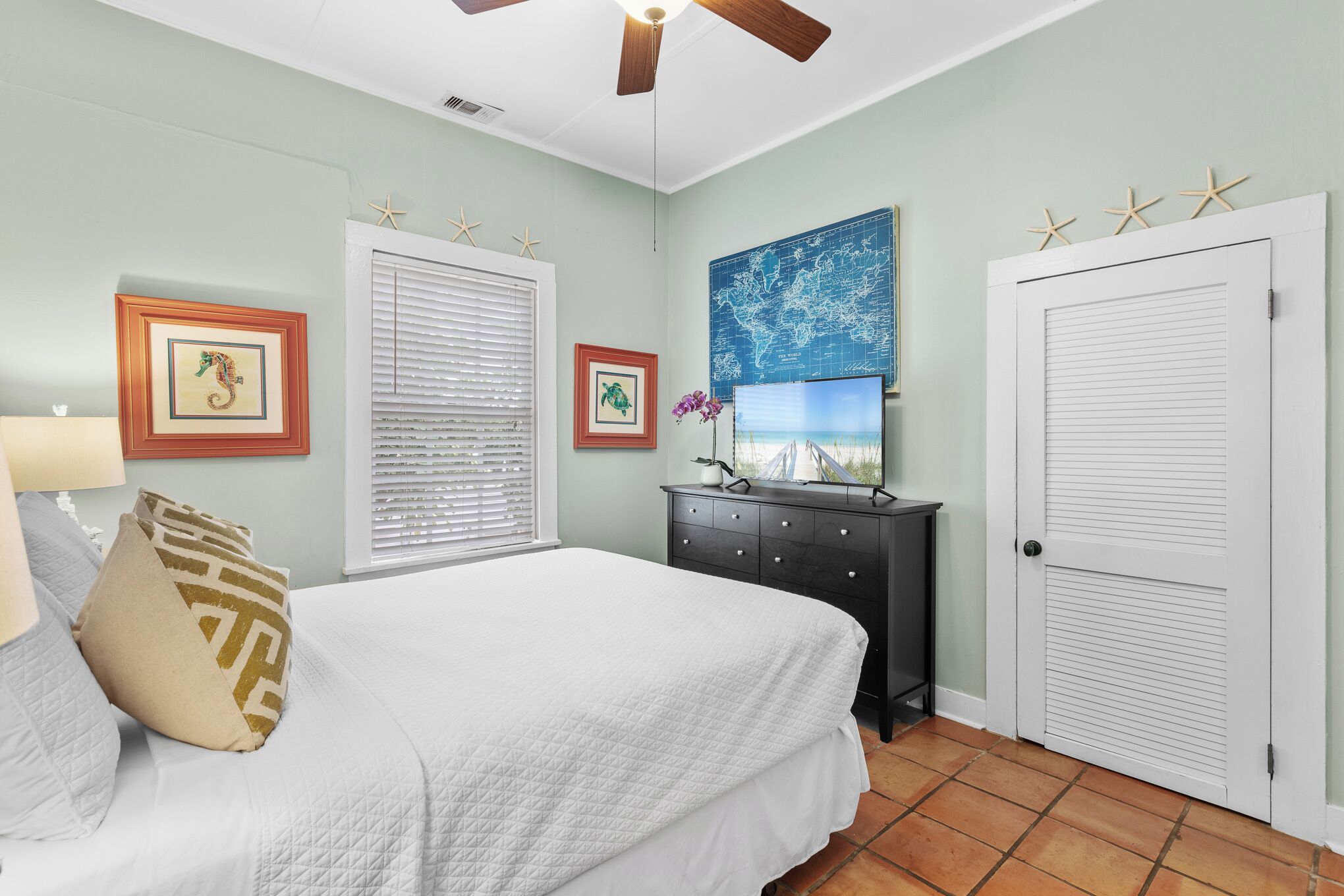 A bedroom with a bed, a dresser, a world map on the wall, and a door with starfish decorations.