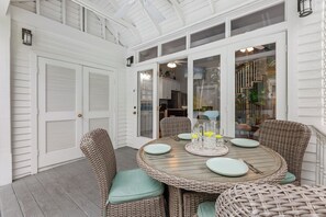 A covered patio with wicker furniture, a round table set for four, and a glass door leading to an interior space. - LOST SHAKER OF SALT ~ 3 Bed, 2 Bath Pet Friendly with 40' Private Heated Pool (Key West)