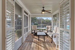 Une véranda couverte avec un ventilateur de plafond, deux chaises, une table et une vue sur un lac.