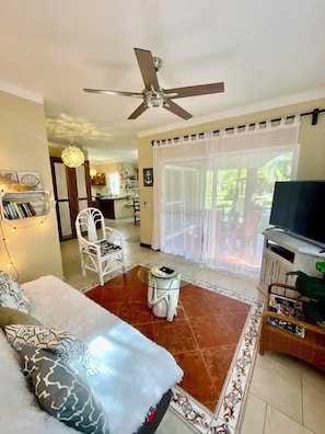 A living room with a ceiling fan, a TV, a sofa, a chair, and a dining area with a table and chairs. - Beautiful 2 Bdrs. Villa with Pool & Beach, 1 minute, Wi-Fi, Chef & Staff (PLAYA DEL SECRETO)