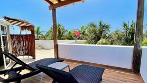 Un espacio de estar al aire libre techado, con sillones reclinables y una mesita, con vistas a un paisaje de palmeras.