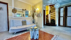 Un salón con un sofá blanco, una mesa de centro de vidrio y una escalera que lleva a un balcón.