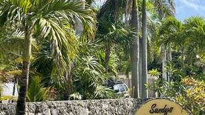Un muro de piedra con un letrero que dice "Sandys Villa" frente a un exuberante jardín con palmeras.
