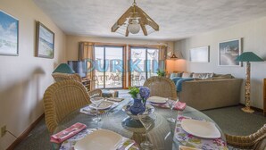 A dining area with a glass table set for four, surrounded by wicker chairs.