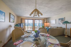 A dining area with a glass table set for four, surrounded by wicker chairs.