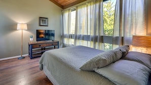 Een slaapkamer met een groot bed, een televisie op een houten dressoir en een raam met dunne gordijnen.