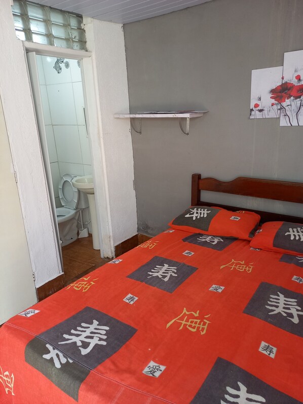 A bedroom with a bed, a wooden headboard, a small shelf, and a bathroom visible through an open door. - Country house/farm in Peruíbe with adult and children's swimming pool, sauna and hot tub. (Estância Antonio Novaes)