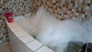 A bathtub with a checkered tile wall, a pink bucket, and a person submerged in bubbles. - Country house/farm in Peruíbe with adult and children's swimming pool, sauna and hot tub. (Estância Antonio Novaes)