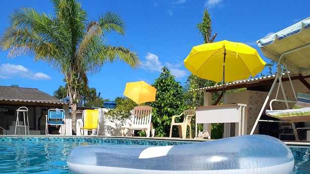 A swimming pool with inflatable floatation devices, lounge chairs, and yellow umbrellas. - Country house/farm in Peruíbe with adult and children's swimming pool, sauna and hot tub. (Estância Antonio Novaes)