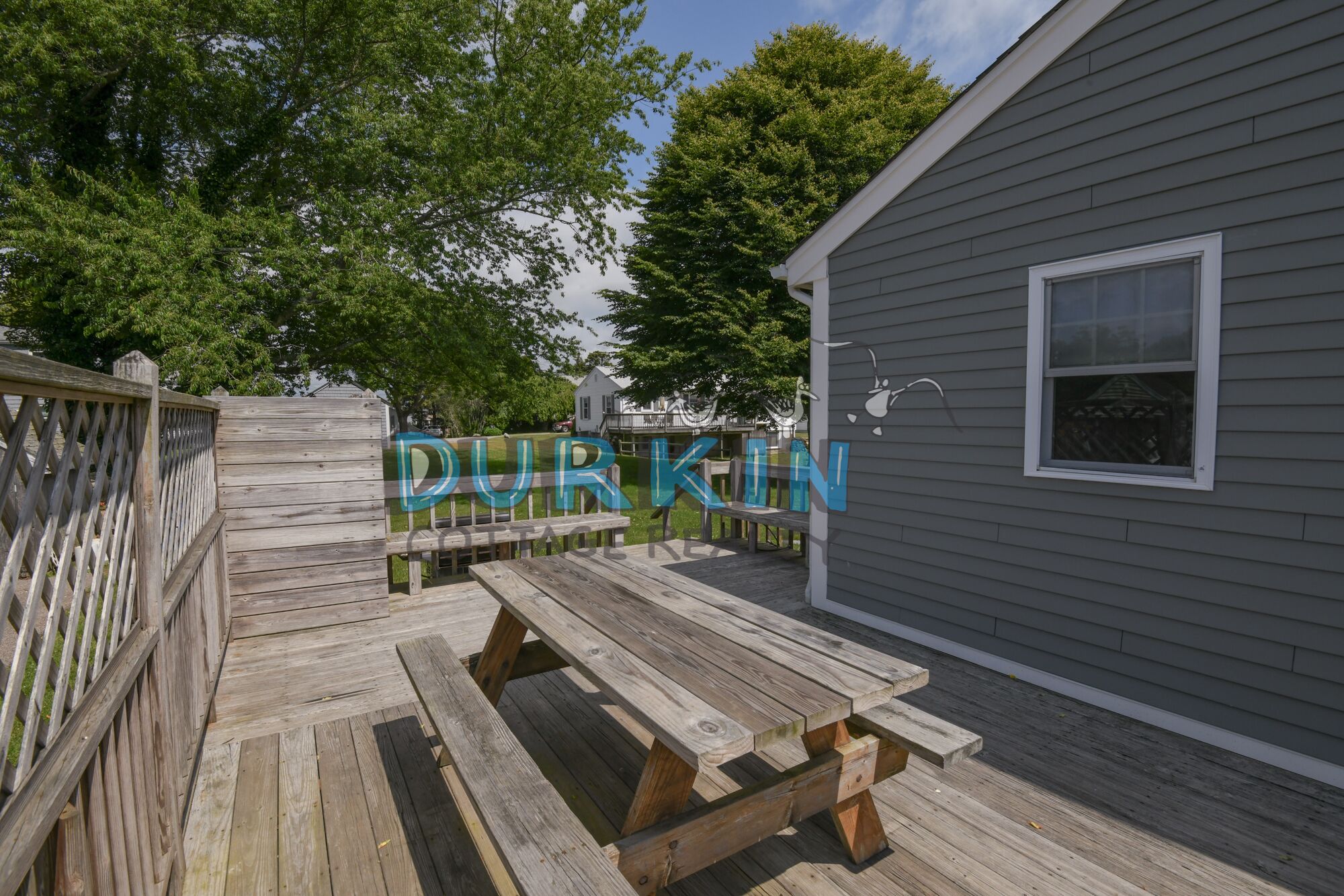A wooden deck with picnic tables, a grey building with a window, and a fence.