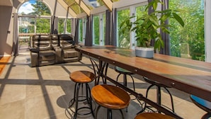 A modern living room with a leather sofa, wooden bar stools, and a large potted plant.