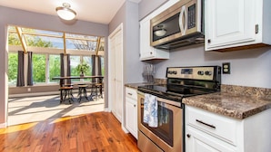 A modern kitchen with a large window, wooden flooring, and stainless steel appliances.