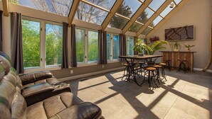 A sunroom with a glass ceiling, leather sofa, dining table, chairs, and potted plants.