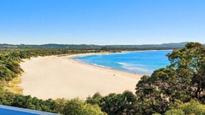 Ein Strand mit klarem, blauem Wasser, sandigem Ufer und dichter Vegetation.