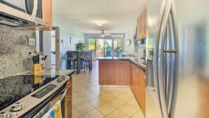 Una cucina con frigorifero in acciaio inossidabile, forno a microonde e fornello. C'è un'area pranzo con tavolo e sedie. La cucina presenta mobili in legno e pavimento piastrellato.