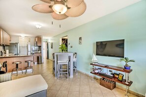 A modern kitchen with a dining area, a TV mounted on the wall, and a ceiling fan.