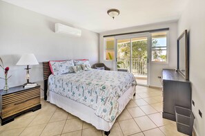 A bedroom with a bed, bedside table, lamp, and a view of the outside balcony.