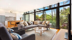 A modern living room with a grey sectional sofa, a round coffee table, and a view of a lush garden through large windows.