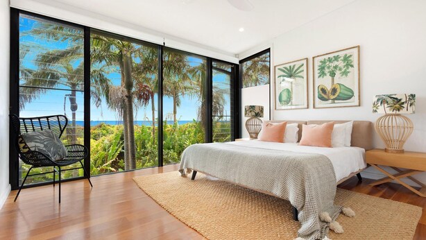 A bedroom with a large window, a bed, a chair, and tropical-themed artwork.