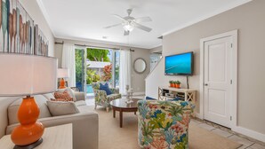 A living room with a sofa, armchair, and coffee table, a ceiling fan, a TV, and a door. - MANGO MARGARITA~ 2 bedroom/2.5 bath, heated private pool, and close to Duval! (Key West)