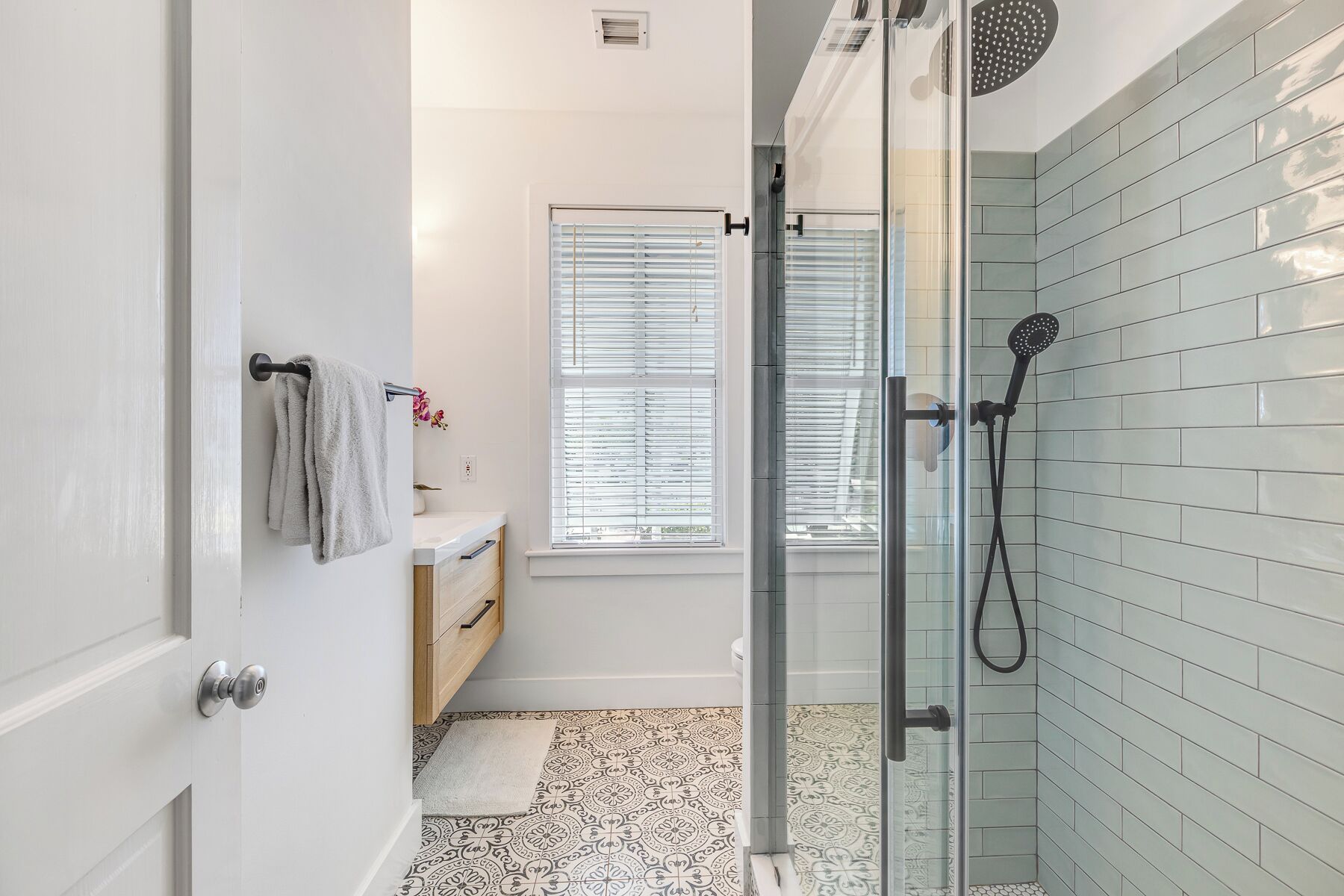 Une salle de bain moderne avec une douche à parois de verre, un lavabo blanc et une fenêtre équipée de stores.