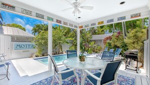 A poolside area with a glass table and chairs, surrounded by tropical plants and a view of the sky. - MANGO MARGARITA~ 2 bedroom/2.5 bath, heated private pool, and close to Duval! (Key West)
