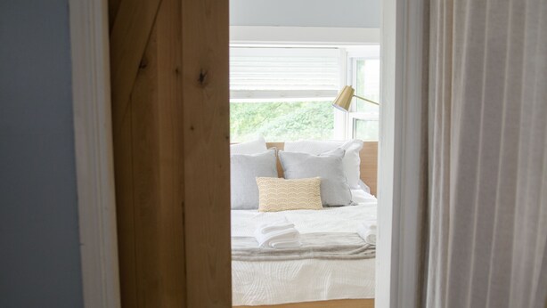 Een slaapkamer met een bed, kussens, een lamp en uitzicht op groen.