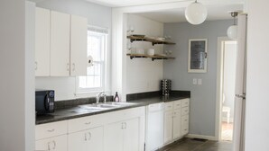 Een moderne keuken met witte kasten, een granieten aanrecht, een inbouw vaatwasser, en een raam dat voor natuurlijk licht zorgt.