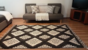 A living room with a grey sofa, patterned throw pillows, a dark and light patterned rug, and a television on a wooden cabinet. - ME MATES PLACE CLOSE TO THE BEST BEACHES THROUGH OUT THE ESPERANCE REGION,. (Condingup, ESPERANCE)