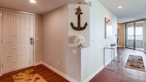 A hallway with a white door, a wall-mounted anchor decoration, a small table with a vase of flowers, and a patterned rug. - Ocean View Condo Pool Spa Gym Tennis  (Del Mar)