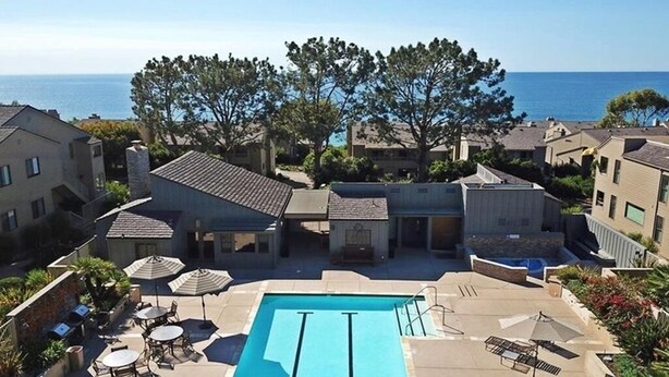 A pool area with a clear view of the ocean, surrounded by buildings and trees. - Ocean View Condo Pool Spa Gym Tennis  (Del Mar)