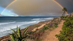 A coastal path with a rainbow over the ocean, surrounded by vegetation and a building in the background. - Ocean View Condo Pool Spa Gym Tennis  (Del Mar)