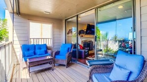 A covered outdoor area with wicker furniture and a glass door leading to a room with a fireplace. - Ocean View Condo Pool Spa Gym Tennis  (Del Mar)