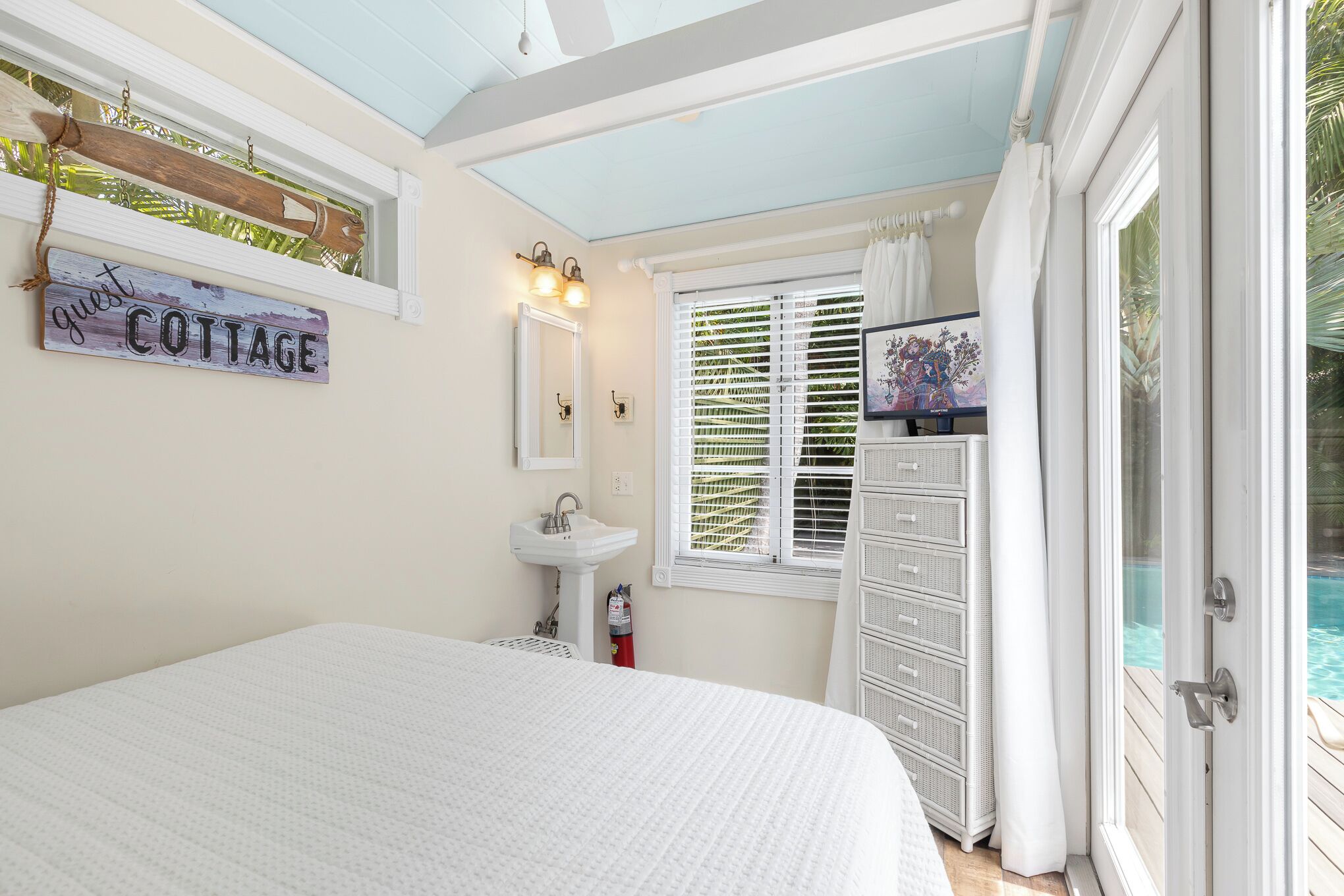 A bedroom with a bed, a white dresser, a sink, and a window with blinds.