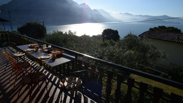 Une terrasse avec une table dressée pour le dîner, donnant sur un lac et offrant une vue sur des montagnes en arrière-plan.