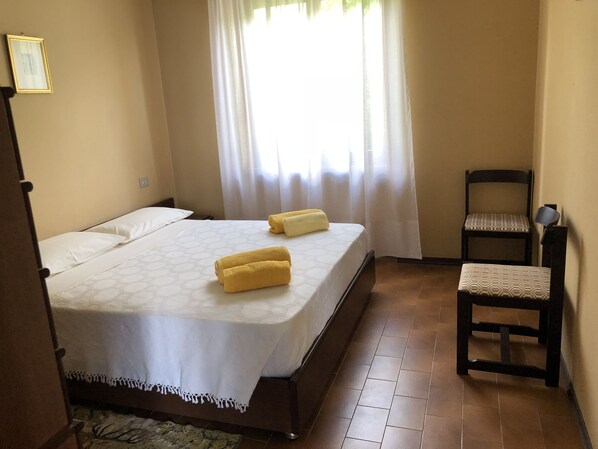 Une chambre à coucher avec un lit, deux serviettes, une chaise et une fenêtre avec des rideaux.