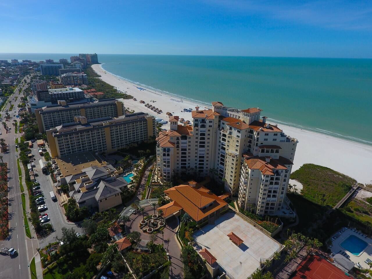 A coastal hotel complex with multiple buildings, a beach, and a swimming pool.